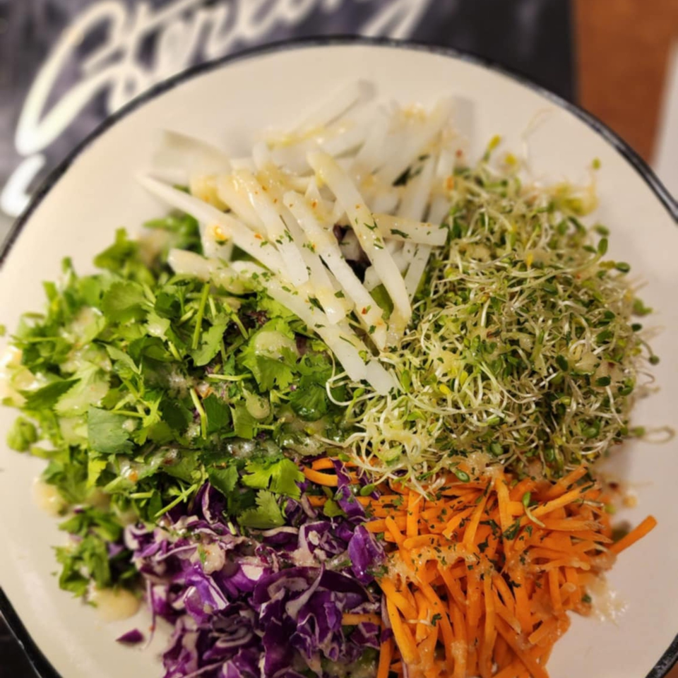 A vibrant salad with cilantro, purple cabbage, shredded carrots, daikon radish, and alfalfa sprouts.