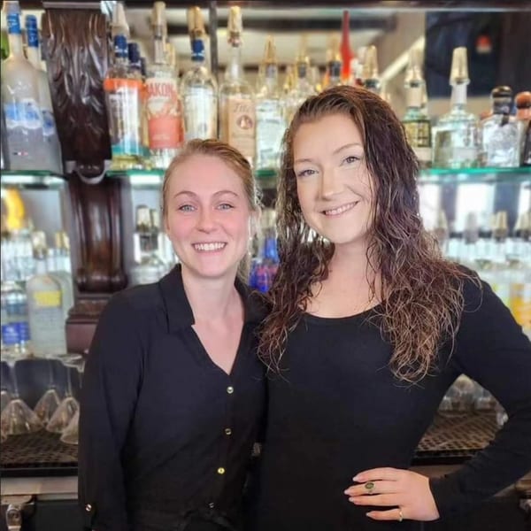 Two smiling Sterling's Restaurant staff members in black shirts stand in front of a bar.