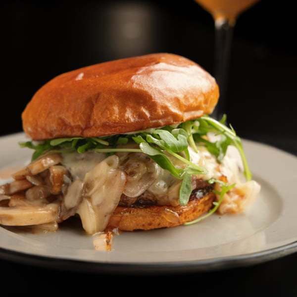 A gourmet burger with melted cheese, sautéed mushrooms, and arugula on a brioche bun.
