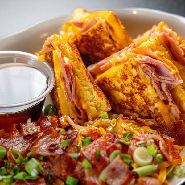 Sterling's Monte Cristo sandwich with ham, cheese, and syrup, served with bacon and green onions.