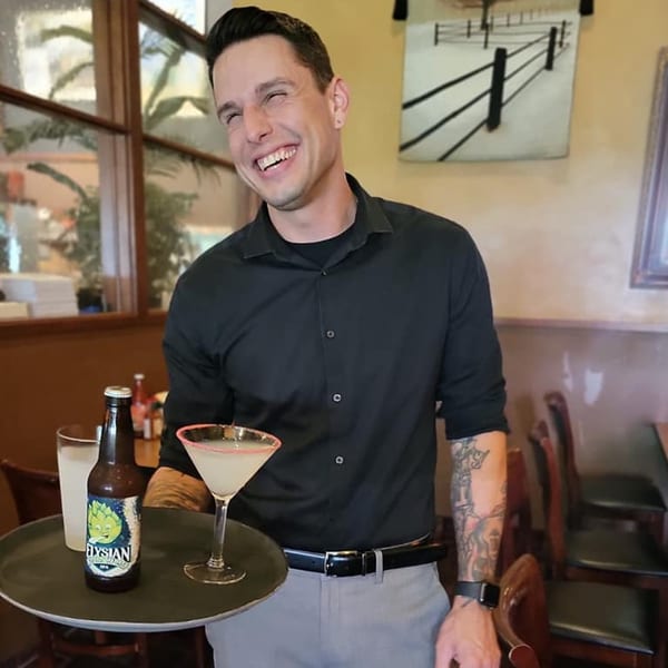 A smiling Sterling's Restaurant server holds a tray with a cocktail and beer bottle.