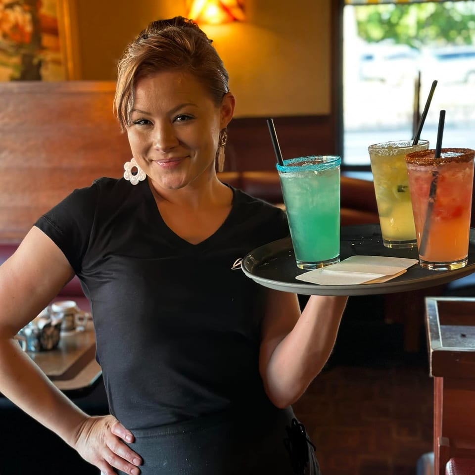 Smiling Sterling's Restaurant server holding a tray with three colorful margaritas.