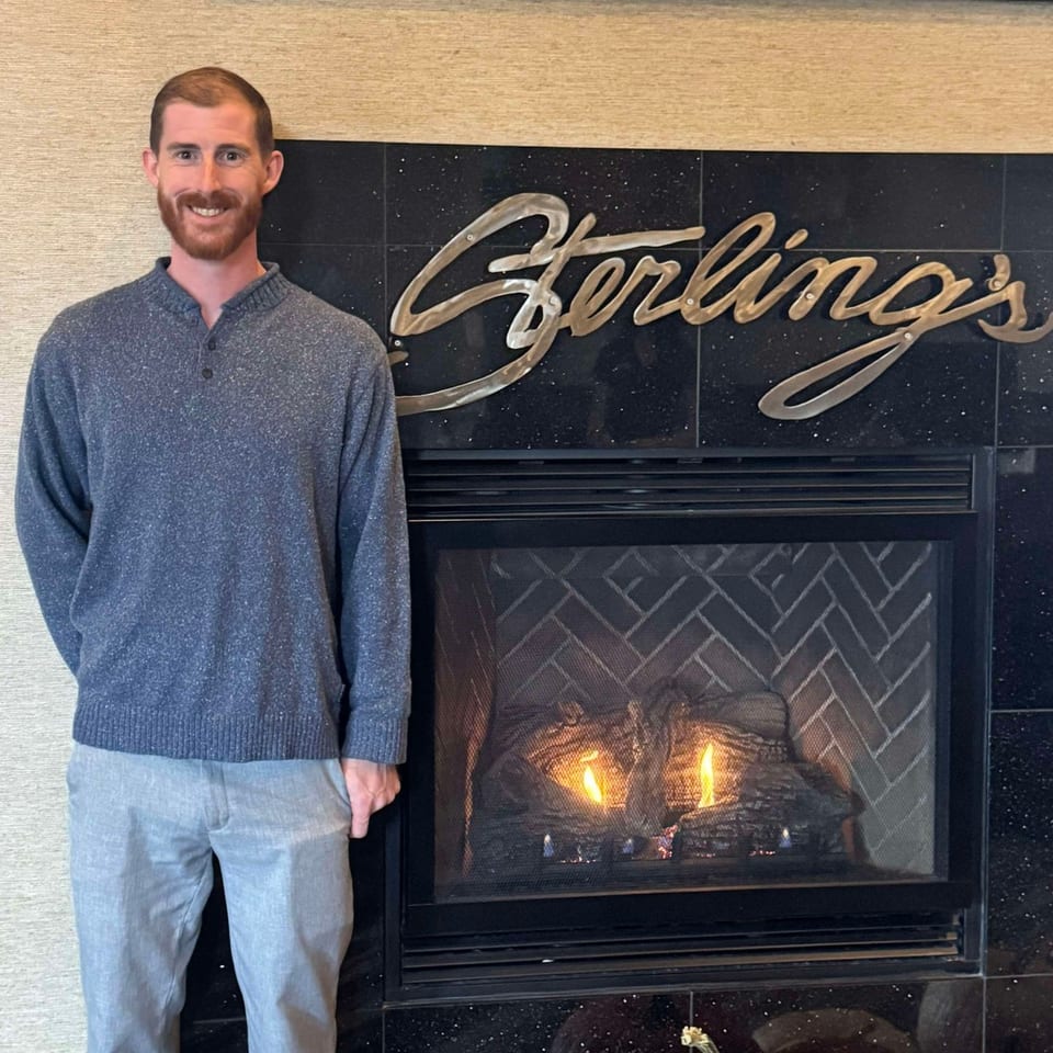 Smiling man standing next to a fireplace with the Sterling's logo above it.