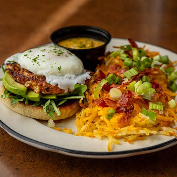 Sterling's breakfast plate with a poached egg, avocado, and hash browns topped with bacon and scallions.