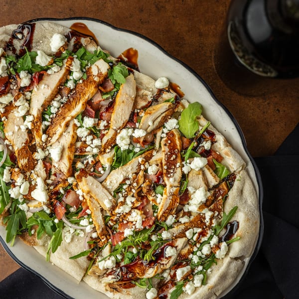 Overhead view of a Sterling's breakfast flatbread with chicken, bacon, arugula, and feta cheese.