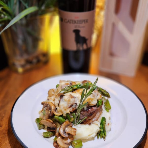 Sterling's Restaurant's steak and mashed potatoes with mushrooms, asparagus, and rosemary, with a wine bottle in the background.