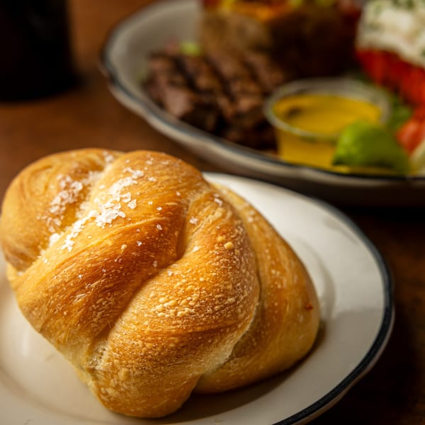 Close-up of a golden-brown, braided bread roll sprinkled with sea salt on a white plate.