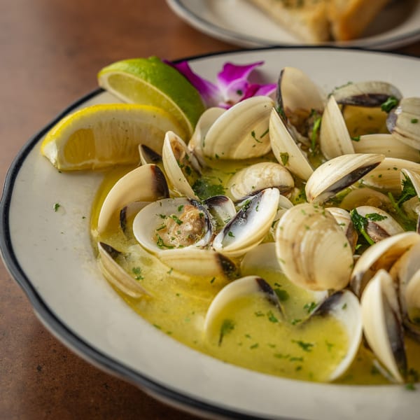 Steamed clams in a buttery broth with lemon and lime wedges, garnished with a purple orchid.