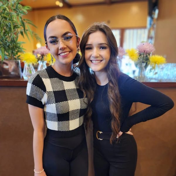 Two smiling young women pose together in Sterling's Restaurant, with flowers and plants in the background.