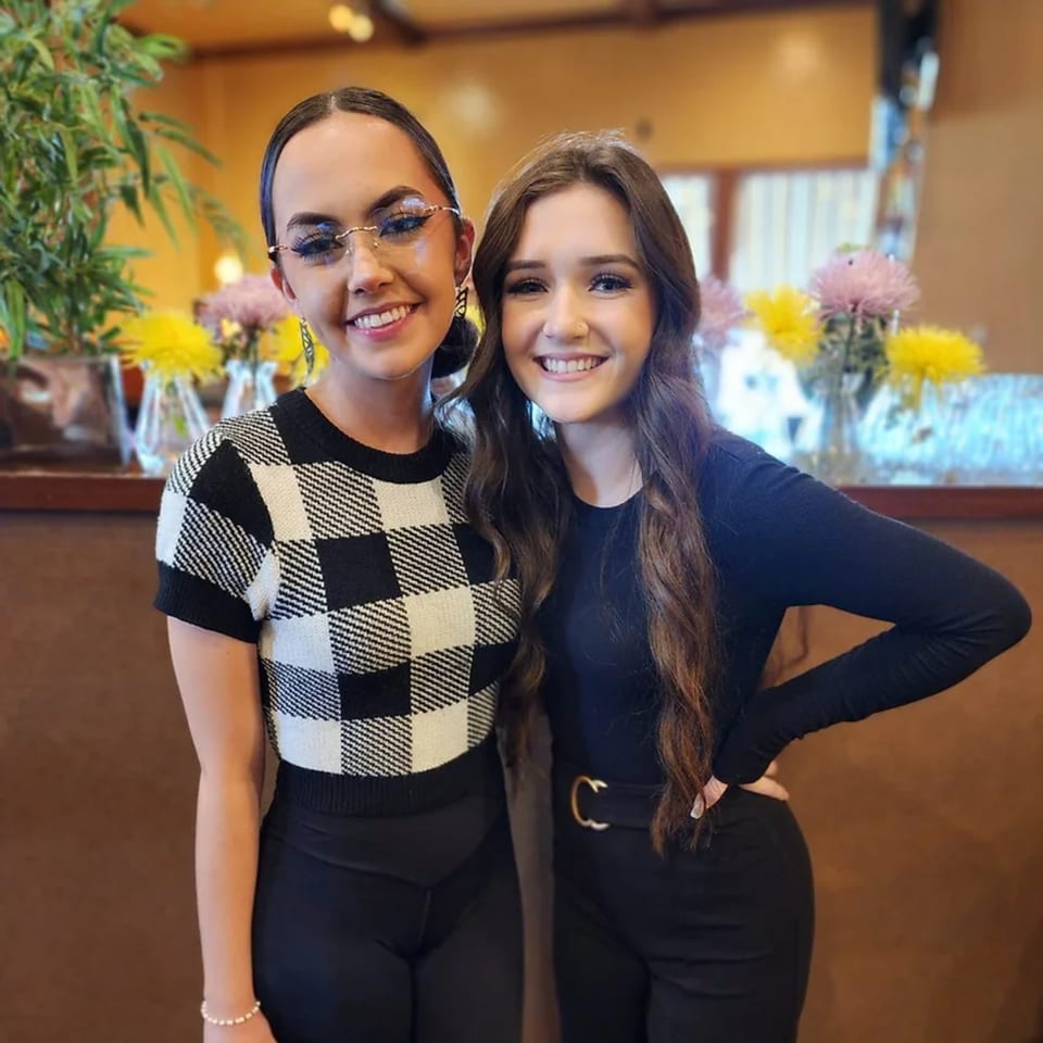 Two smiling young women pose together in Sterling's Restaurant, with flowers and plants in the background.