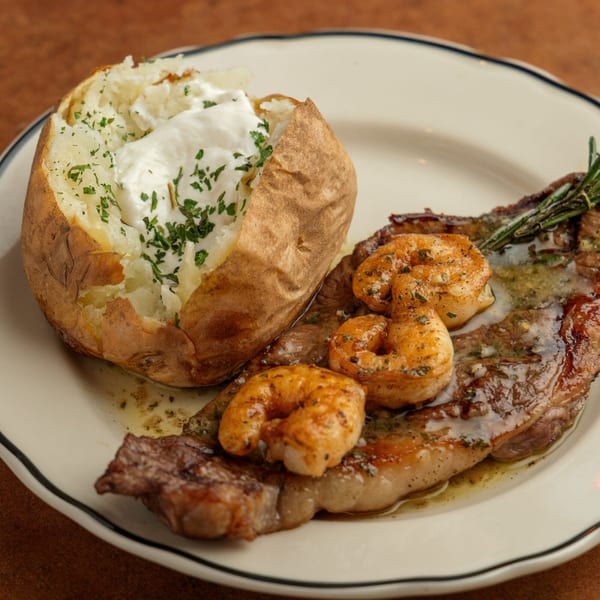Sterling's surf and turf with steak, shrimp, and a loaded baked potato on a white plate.