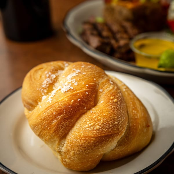 A golden-brown, braided bread roll, sprinkled with sea salt, rests on a white plate.