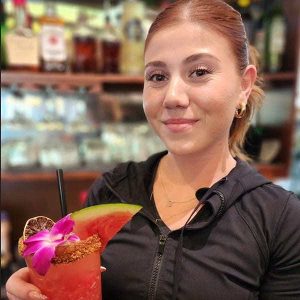 A smiling Sterling's Restaurant server holds a watermelon cocktail garnished with a flower and lime.