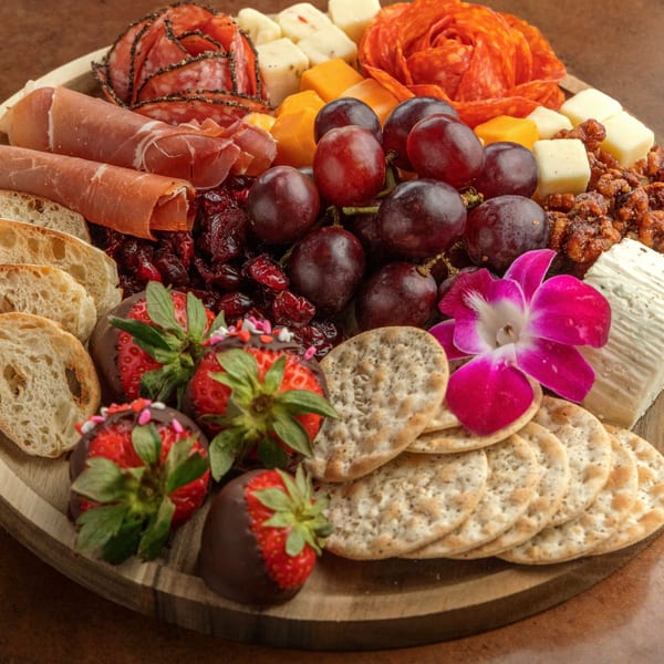 A charcuterie board with meats, cheeses, grapes, chocolate-covered strawberries, crackers, and bread.