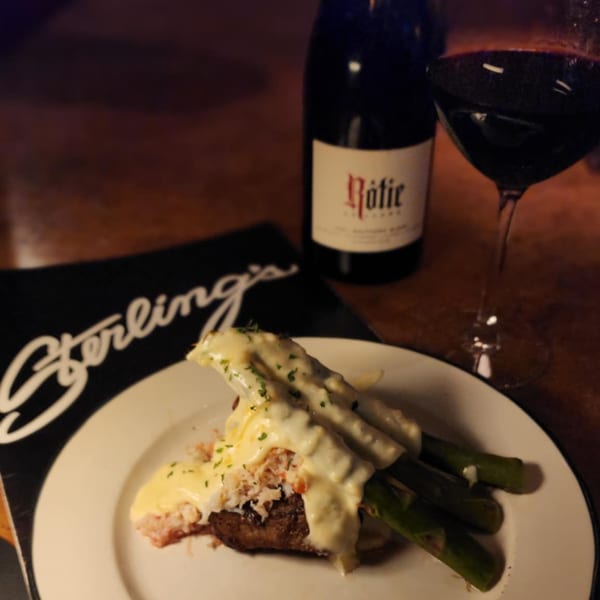 Sterling's breakfast dish with asparagus, crab, and hollandaise sauce, alongside a bottle and glass of red wine.